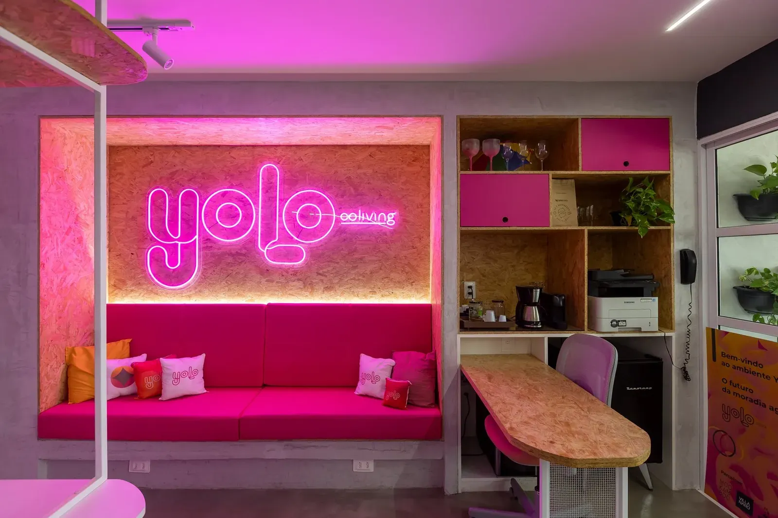 Área de convivência corporativa com letreiro luminoso e sofá rosa